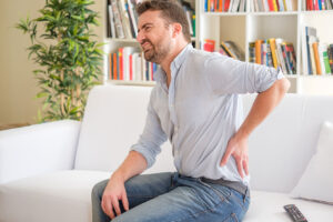 Man sitting on couch holding his back in pain